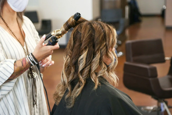 A hairstylist using a curling iron on a client in a salon Organic Beauty Salon
